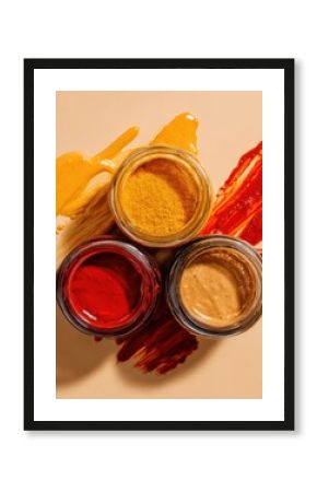 Three jars with colorful sauces and spices on beige background, red, yellow and brown pastes smeared under jars. Top view food styling photography. Culinary and seasoning concept. 