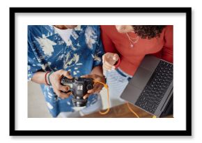 Young adult Black woman and young adult Black man reviewing digital camera images together while holding laptop, collaborating on food photography project, hands and torsos visible