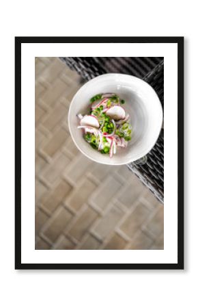Fresh vegetable salad with sliced radishes, peas, and green onions in a white bowl on a wicker chair, top view, healthy and colorful food presentation.