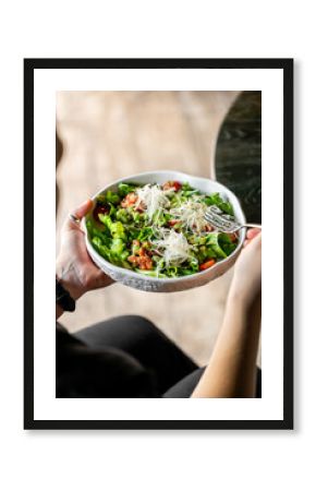 Close-up of a person holding a bowl of fresh salad with lettuce, cherry tomatoes, shredded cheese, and a fork, representing healthy eating and vibrant food textures.