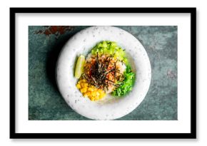 Colorful poke bowl with rice, fresh vegetables, seaweed salad, lime wedge, and spicy sauce, garnished with sesame seeds on a ceramic plate. Healthy and vibrant Asian dish.