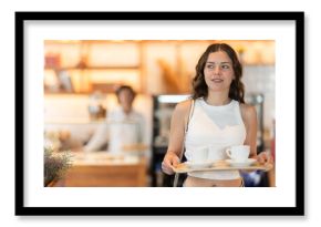 Young woman carrying tray with coffee cups to table in cafe