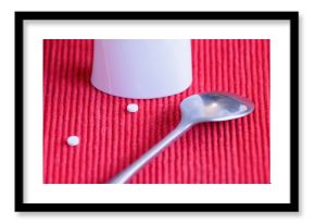 sweetener tablets Small white pills beside a silver spoon on a red textured surface in a kitchen setting