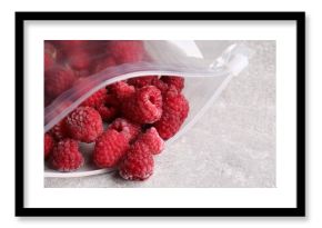 Ripe frozen raspberries in open zipper bag on grey textured table, closeup