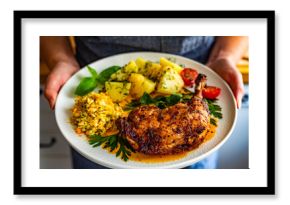Woman holding plate with oven roasted chicken leg with boiled potatoes and young cabbage salad, close-up