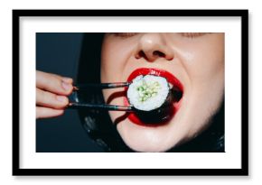 Woman with red lips holding sushi with chopsticks, showcasing enjoyment and modern cuisine in a stylish, vibrant setting.