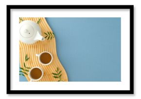 Elegant tea set on wooden tray with green leaves. Minimalist top view against pastel blue.