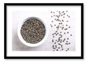Puy lentils in a white bowl on linen. Dried variety of small lentils, mottled, of slate-gray to dark green color, with blue marbling. Lens esculenta variety, grown in the Auvergne region of France.