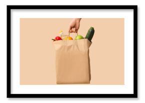 Woman holding paper bag with vegetables, fruits and bottle of oil on beige background
