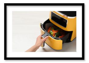 Woman opening air fryer with grilled vegetables at white wooden table, closeup. Space for text