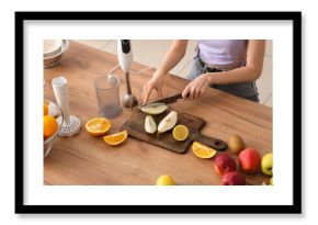 Young woman cutting fresh pear for smoothie in kitchen