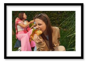 Young woman biting burger with passion while friends laugh nearby. Concept of authentic emotion, youth lifestyle, food realism for street-food branding, social content, and lifestyle marketing.