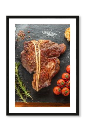 Grilled T-bone steak with seasonings on slate serving plate. Flat lay.