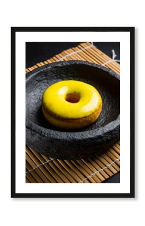 Vivid Yellow Glazed Donut in Black Stone Bowl on Bamboo Mat