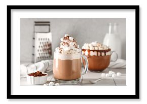 Glass cups of hot cocoa drink with whipped cream and marshmallows on white tile table