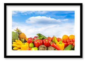 Assorted fresh fruits and vegetables arranged outdoors under blue sky with scattered clouds