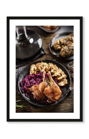 Portion of roast duck leg red cabbage homemade dumplings on plate and red wine on the background