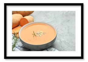 Delicious sweet potato soup with pumpkin seeds in bowl, vegetables and rosemary on grey textured table, closeup. Space for text