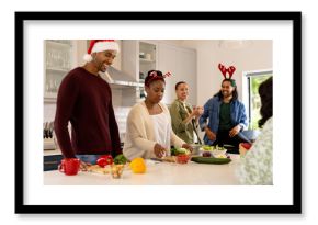 Wearing christmas hats, multiracial friends preparing festive meal in kitchen, spirit, at home