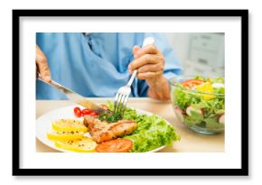 Asian senior woman patient eating pork chop stake and vegetable salad for healthy food in hospital.