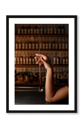 Female hands of a bartender holding a long golden bar spoon for mixing cocktails