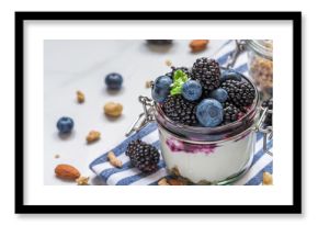 Yogurt parfait with blackberry, blueberry, granola, nuts and berry sauce in glass jar with fresh mint on white background. Layered Greek yoghurt with fresh berries. Healthy breakfast
