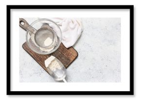 Bowl with flour, metal sieve, scoop and wooden board on light background