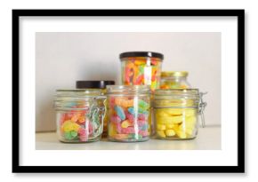 Tasty gummy candies in glass jars on light table, closeup