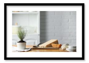 Different types of cheese, slicer and potted thyme on wooden table indoors. Space for text
