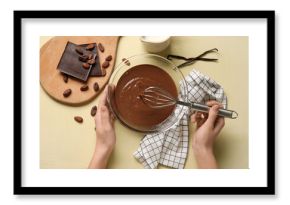 Female hands whisking melted chocolate on beige background. Top view