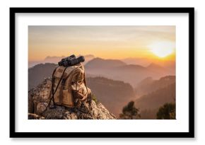 Binocular with backpack on top of rock mountain at sunset