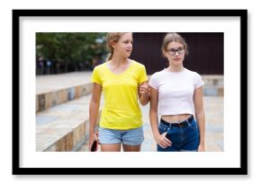 Two teenager girls walking together through park in afternoon.
