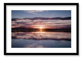 Spectacular landscape with sun setting behind mountains and clouds and reflecting in calm water of river delta with fisherman sticks