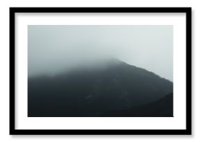 Misty mountain peak shrouded in dense fog on overcast day
