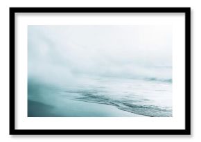 Soft pastel mint and gray mist gently dissolving on a sandy beach with gentle ocean waves rolling in under a pale overcast sky