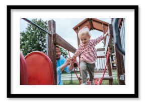 Toddler crossing playground obstacle with dad's support