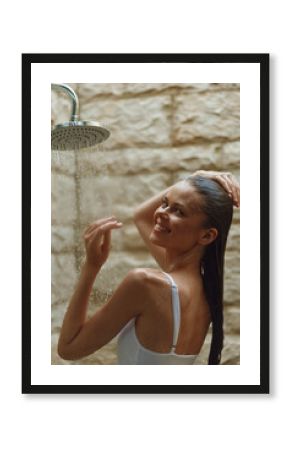 smiling woman enjoying outdoor shower with wet hair, natural stone background, warm lighting, relaxed mood, casual white swimsuit, summer freshness