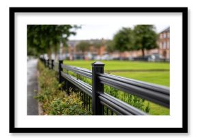 Black metal fence with ornate details lines a green lawn at an industrial park, captured in a side view during springtime