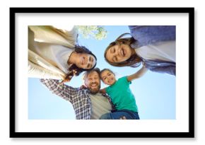 Bottom view of happy young family of four looking cheerful at camera outdoors on blue sky background. Portrait of smiling mother, father and children enjoying time in nature together.