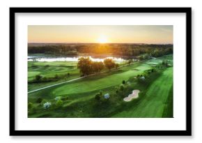 Golf course at sunset with beautiful sky and sand trap. Scenic panoramic view of golf fairway with bunker from drone