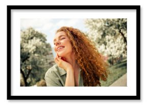 Young red-haired woman enjoying a sunny day outdoors with a beautiful smile in an urban park setting during springtime