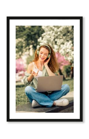 Young woman enjoying music while working outdoors in a park on a sunny day during spring or summer