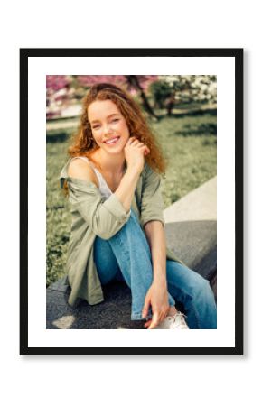Beautiful young woman enjoying a sunny spring day outdoors, sitting relaxed in a park surrounded by blooming flowers