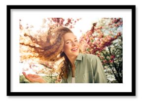 Beautiful young woman smiling joyfully outdoors in a blossoming park under the daylight with vibrant spring colors