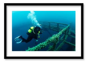 diver diving next to the wreck of a structure submerged in the sea colonized by marine life, concept of scuba diving and underwater adventure
