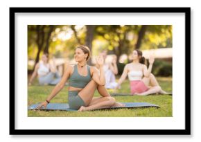 Sporty young girls performing seated twisting asana Matsyendrasana on mat in in a summer park during daily yoga session