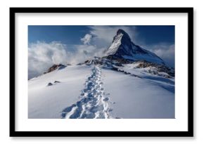 Snow-covered mountain peak with a trail of footprints leading to the summit under a dramatic cloudy sky.