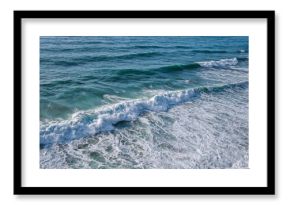 Sea water with foamy surface and waves. Close-up top view of green and blue rushing water near the shore