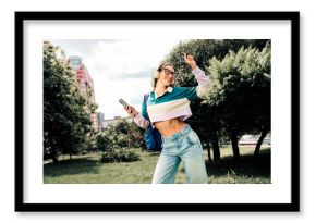 Young woman enjoying music on headphones while dancing happily in an outdoor urban park with bright greenery