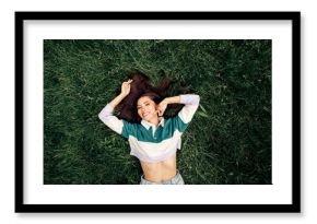 Positive woman relaxing outdoors on grass enjoying a sunny day with a cheerful smile and casual trendy clothing style.